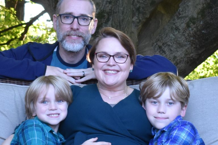 Her hair growing in after chemo treatment, Charlotte Safrit hugs her two children close, her husband behind her, a tree offering them shelter on a beautiful day.