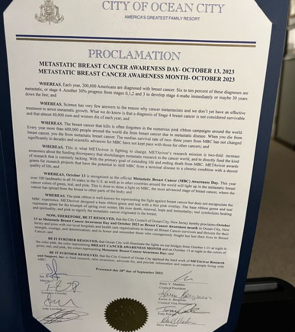 Jeanmarie Mason stands with an advocacy sight for MBC: Educate, advocate, research, cure, as her 4 words for Stage IV breast cancer.