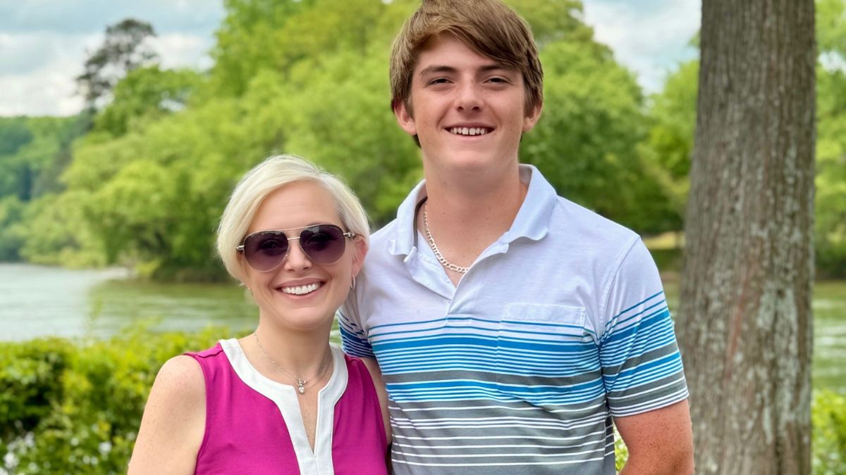 Courtney Bugler stands proudly with her son, a young man, in a beautiful outdoor setting.