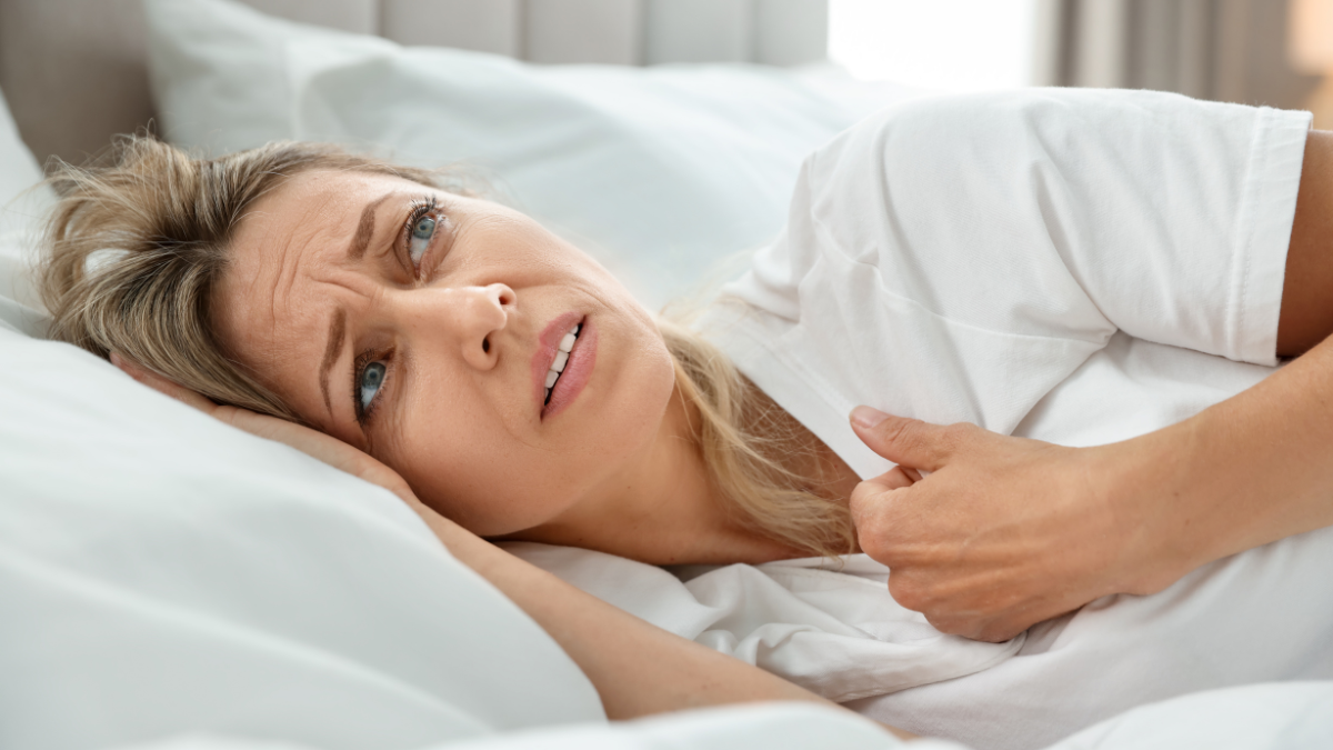 A white woman laying in bed with a distressed look on her face