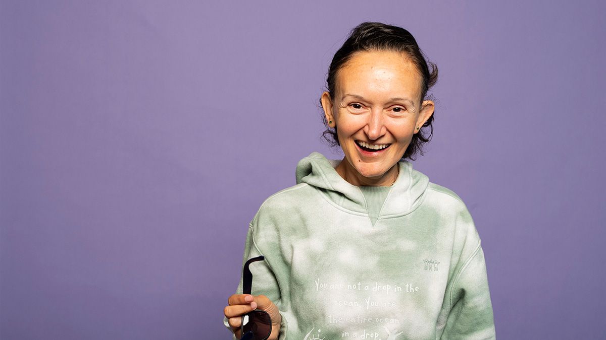 A white woman with short hair smiling in front of a purple background