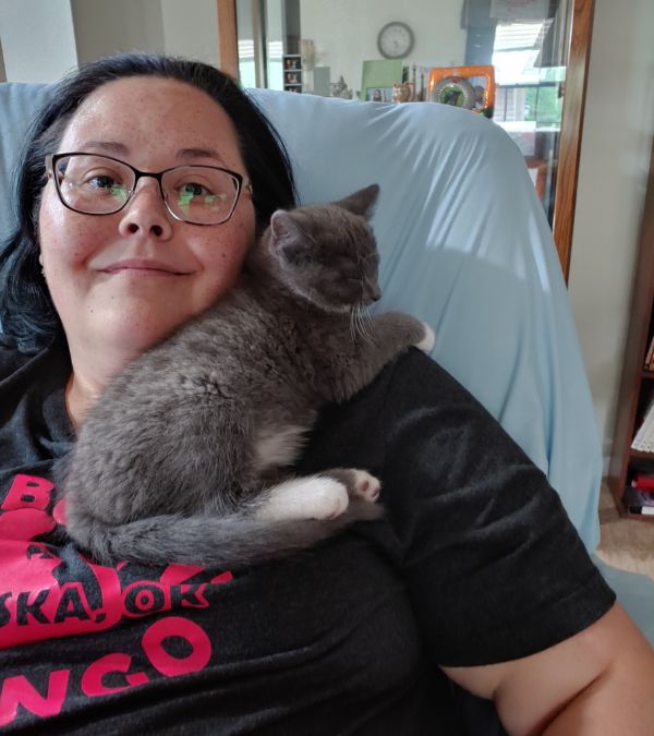 Lisa Walker relaxes on her couch with a gray kitten resting on her shoulder.