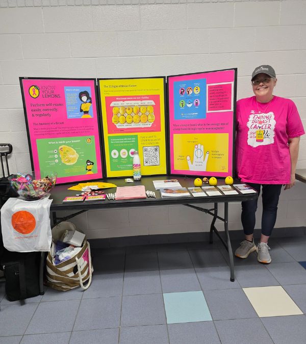 Lisa Walker stands in front of a colorful information table in her advocacy to raise awareness about breast cancer.