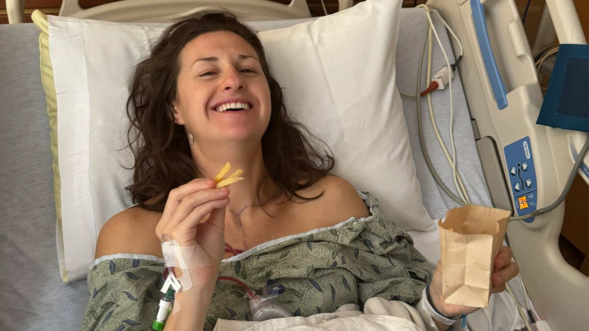 Nicole Beck smiling in a hospital bed and gown holding french fries
