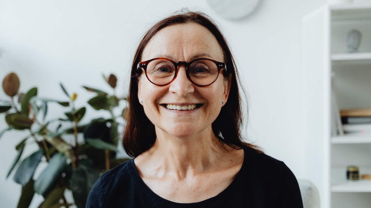 An older white woman with circular glasses, smiling