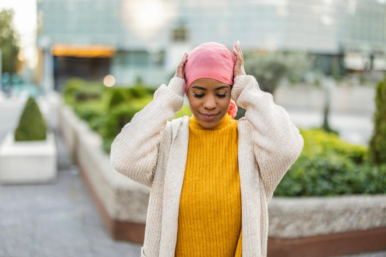 A young Black woman adjusting her pink head wrap