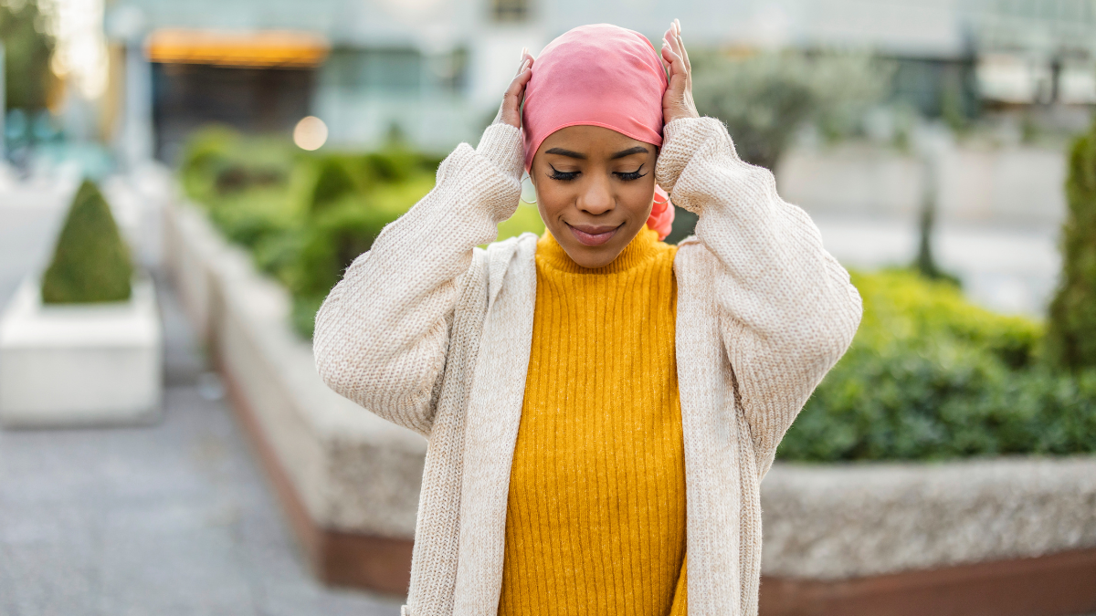 A young Black woman adjusting her pink head wrap