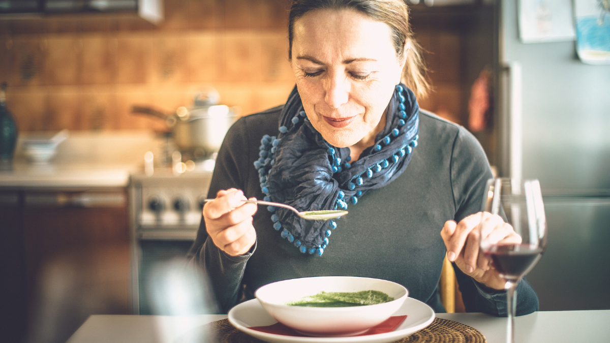 An older white woman blowing on her spoon full of soup