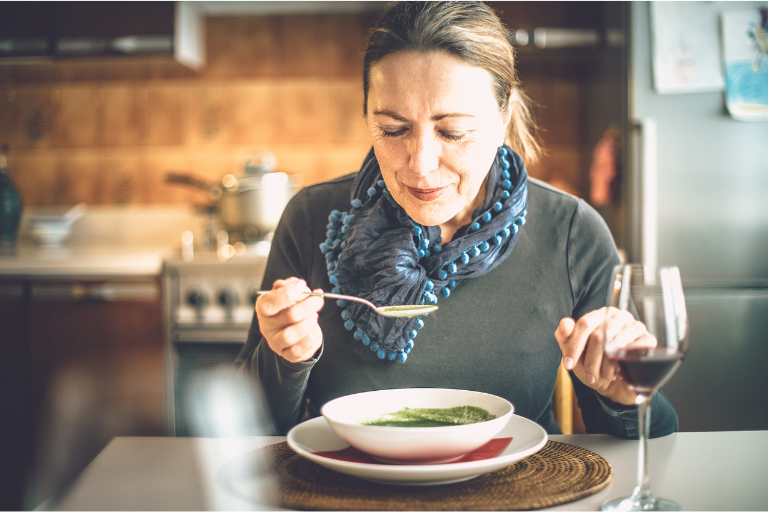 An older white woman blowing on her spoon full of soup