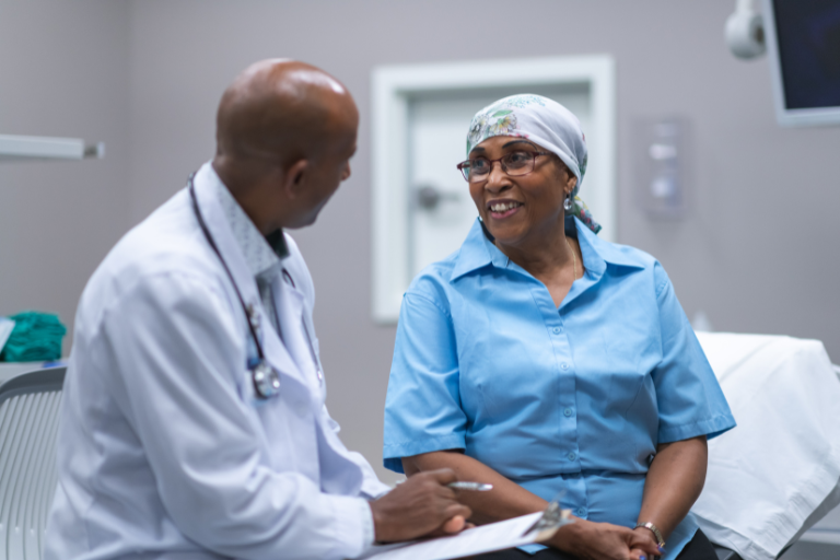A Black woman sitting on the table at the doctor's office, in conversation with her Black male doctor