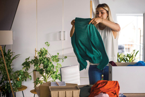 A woman looks at a shirt, with a box full of other clothes ready to donate next to her