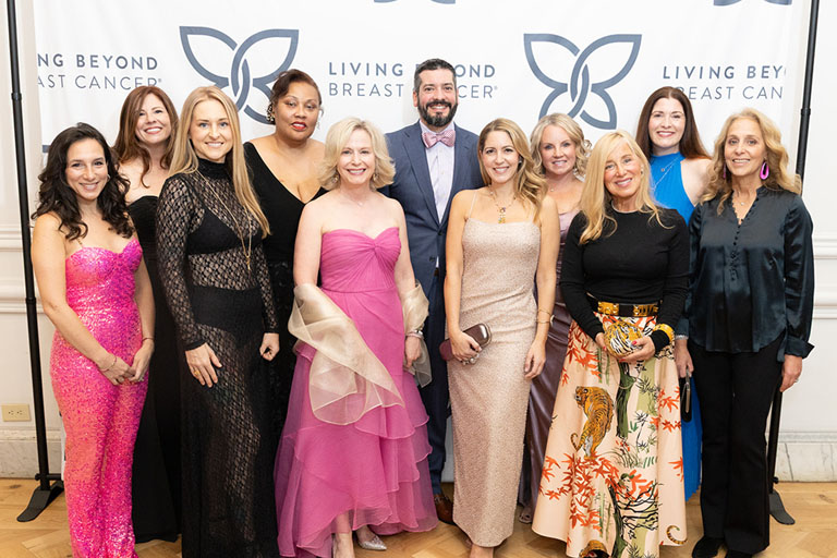A diverse group of women and one man, dressed up, smiling in front of LBBC's step-and-repeat at the 2025 Butterfly Ball