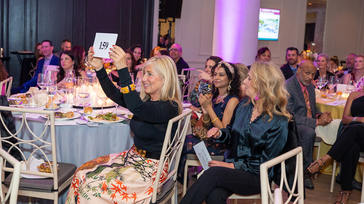 A white woman holding up bidder number "87" to bid during the live auction