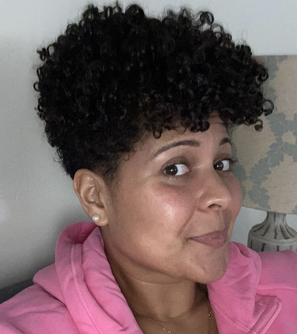 Amara Brown smiling in a selfie wearing a pink sweatshirt with shorter hair.