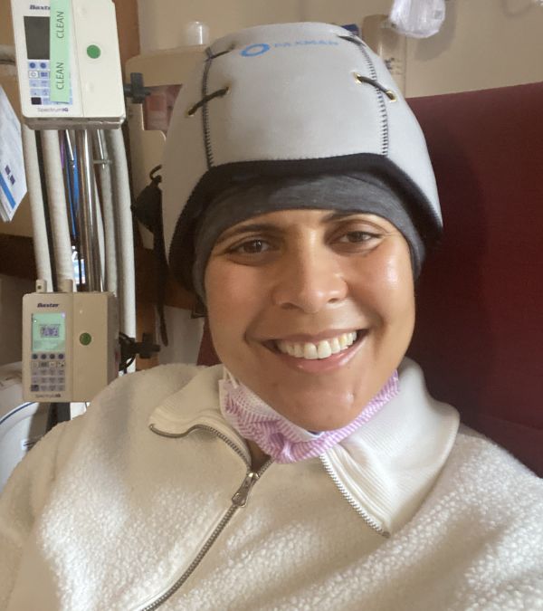 Amara Brown in her chemo infusion chair wearing the Paxman Scalp Cooling cap.