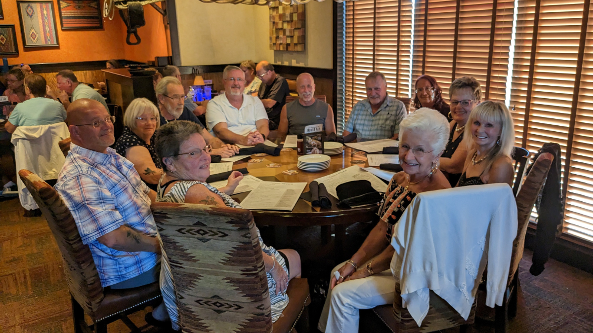 A group of 11 older white people sitting and smiling around a large table at a restaurant