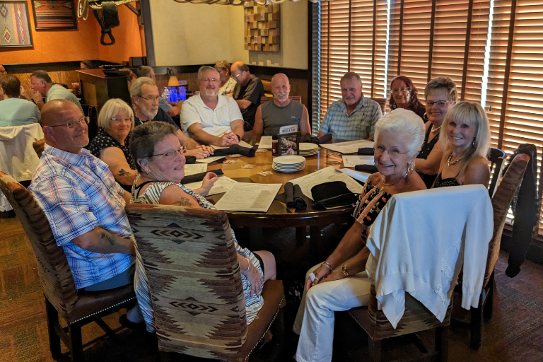 A group of 11 older white people sitting and smiling around a large table at a restaurant