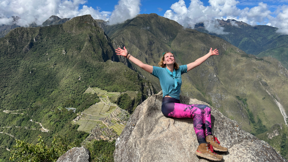 Claudia De Pasquale sitting on top of a rock with her arms out, smiling, on top of Machu Picchu.