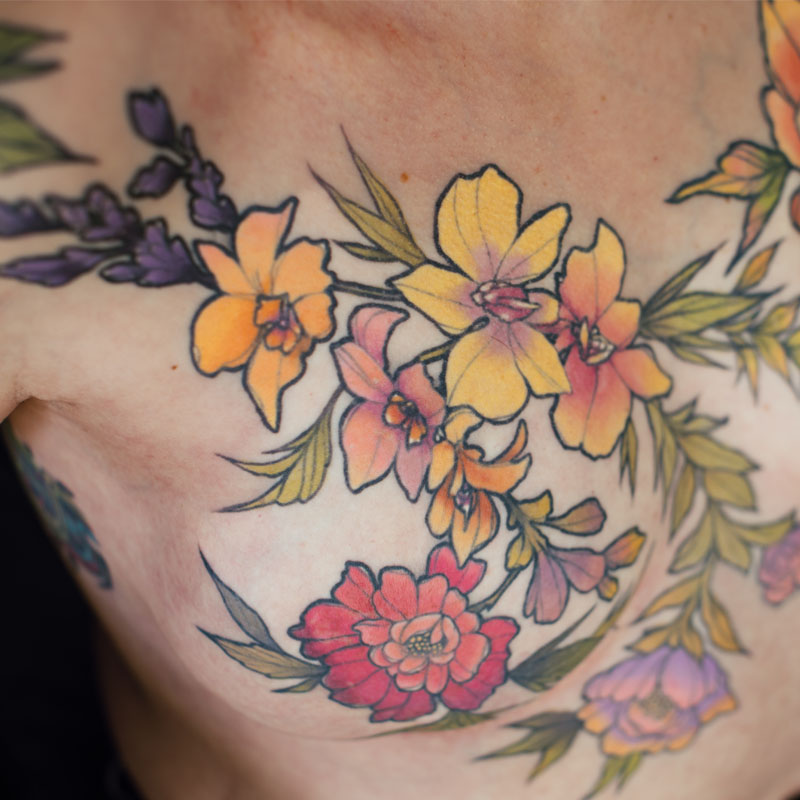 Close up photo of a post-mastectomy floral tattoo covering her chest, shoulders and upper arms.