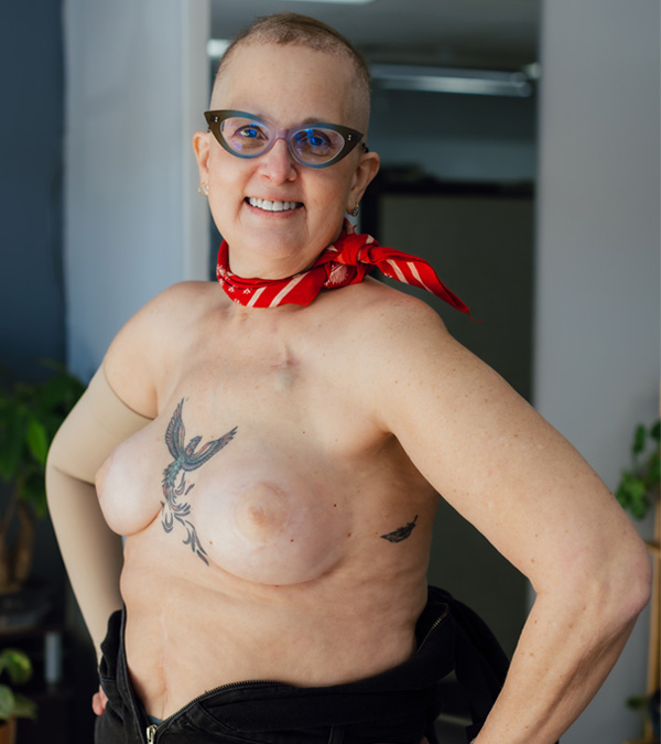 A white woman smiling at camera showing her post-mastectomy tattoo.
