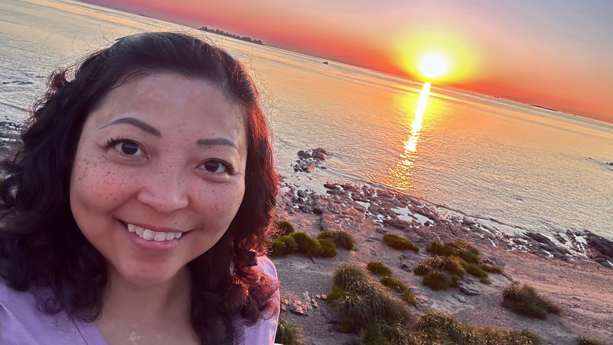 An Asian woman smiling in front of a beach sunset