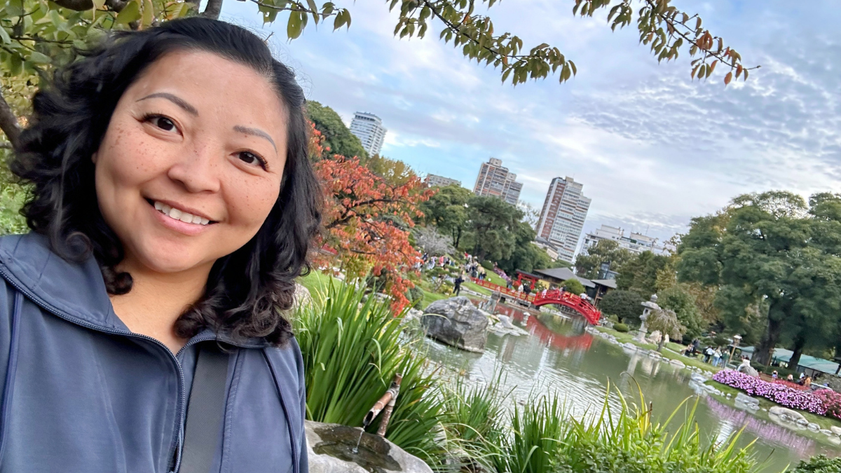 An Asian woman smiling in front of a pond and flowers