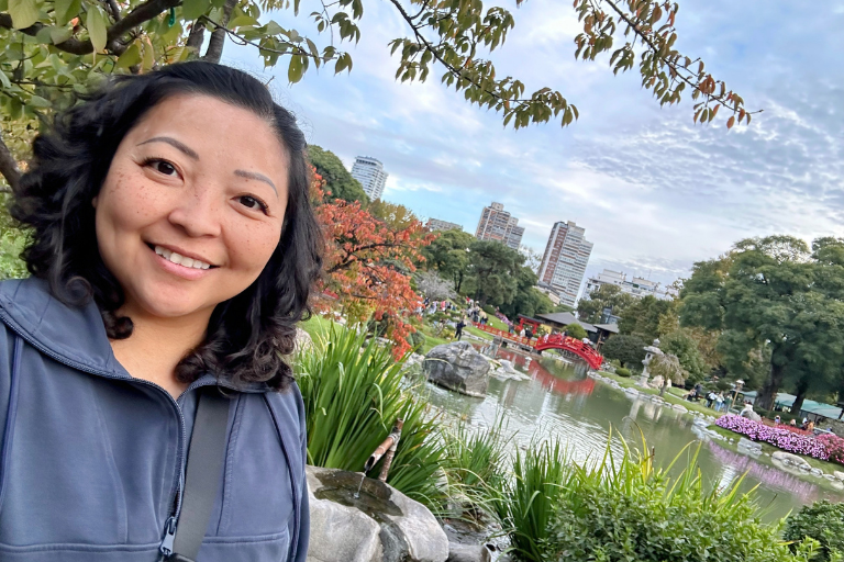 An Asian woman smiling in front of a pond and flowers