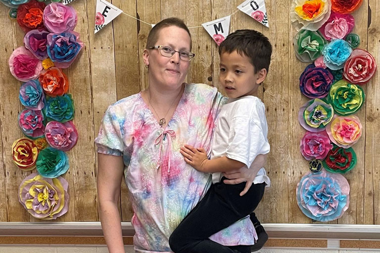Jenny Peterson holding her son in front of a banner that read "We heart mom"