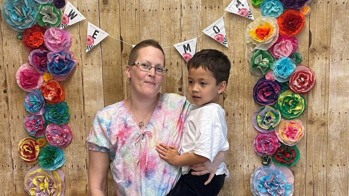Jenny Peterson holding her son in front of a banner that read "We heart mom"