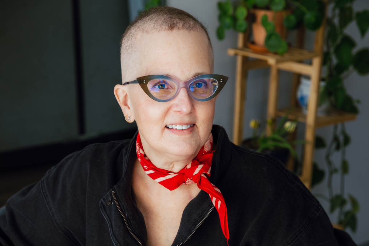 A white woman smiling in a tattoo parlor, wearing a red scarp around her neck