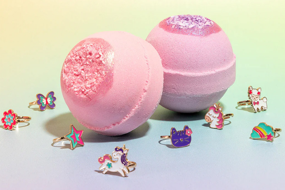 Two pink bath bombs with whimsical cat, unicorn, and star enamel rings around them