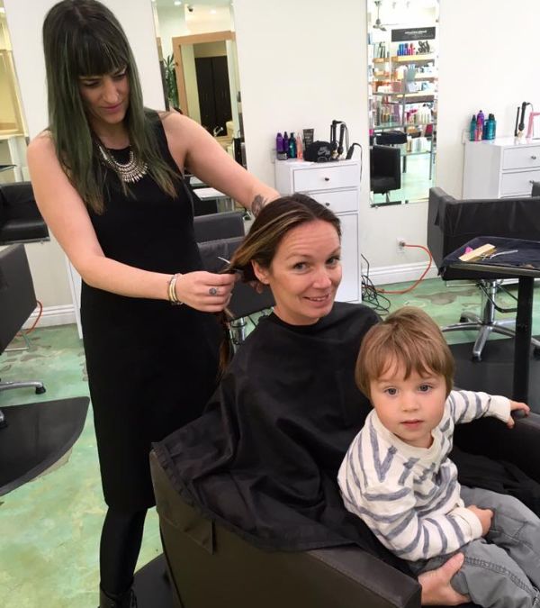 A hairstylist begins to cut Szilvia Gogh's braids, as her young son sits on her lap.