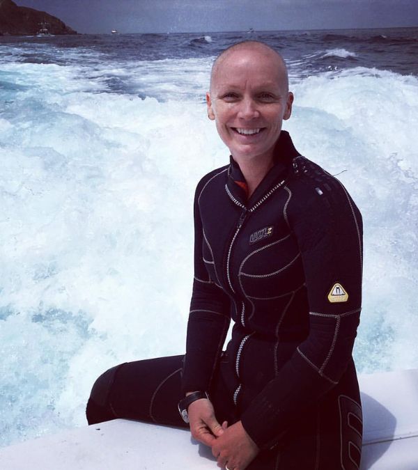 Szilva Gogh sits on a surfboard in the ocean, wearing a wet suit.