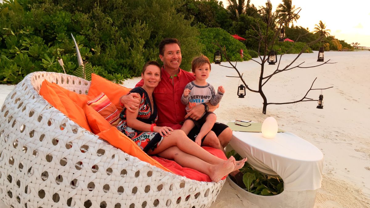 Szilvia Gogh, her husband, and their young son relax on an oversized and colorful beach sofa on the beach in the Maldives.