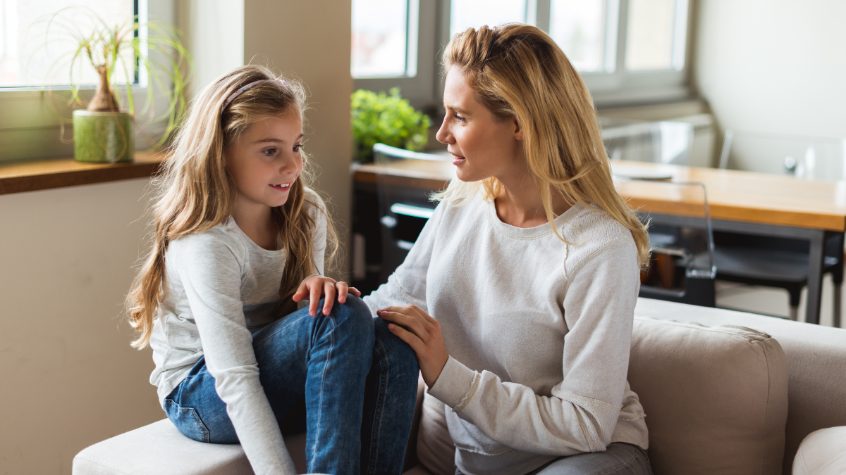 A white woman sitting next to her daughter and engaging in conversation on the couch
