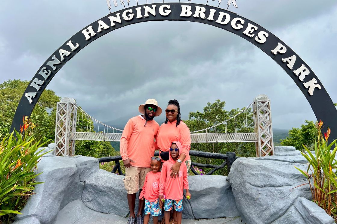 Jonise Louis and her family are dressed casually in coral as they stand under an amusement park arch.