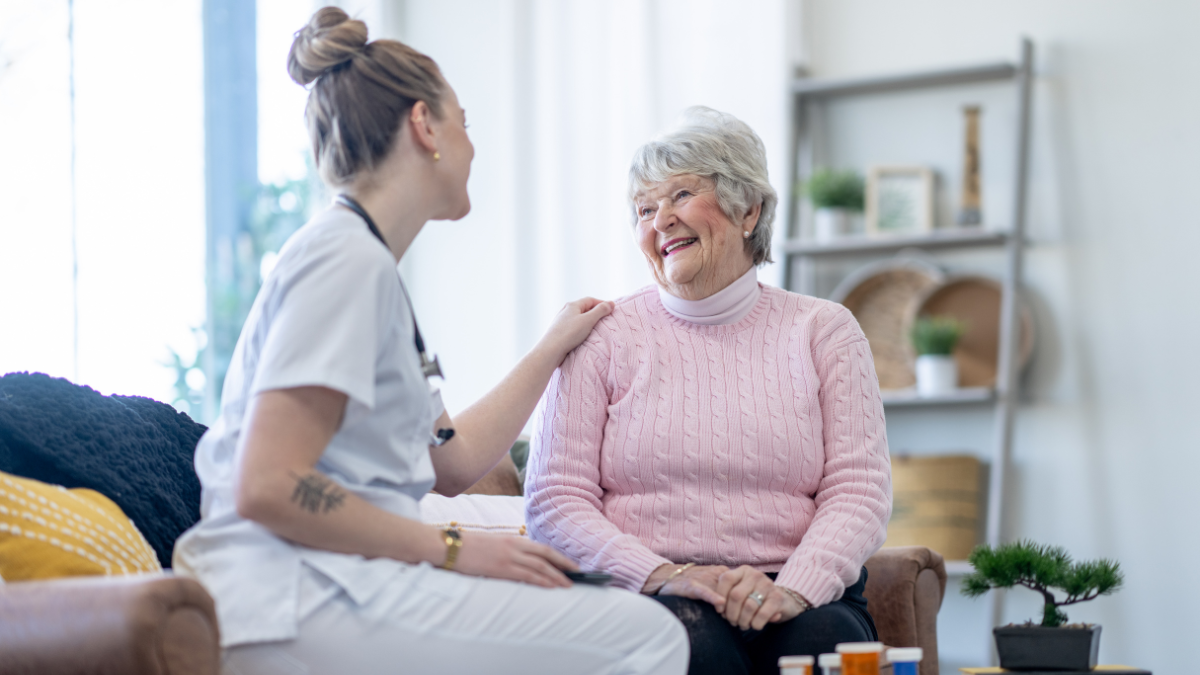 A healthcare worker provides in-home support to an older woman.