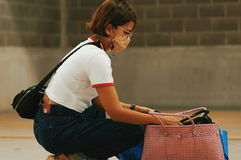 A woman wearing a mask crouched down next to her bag