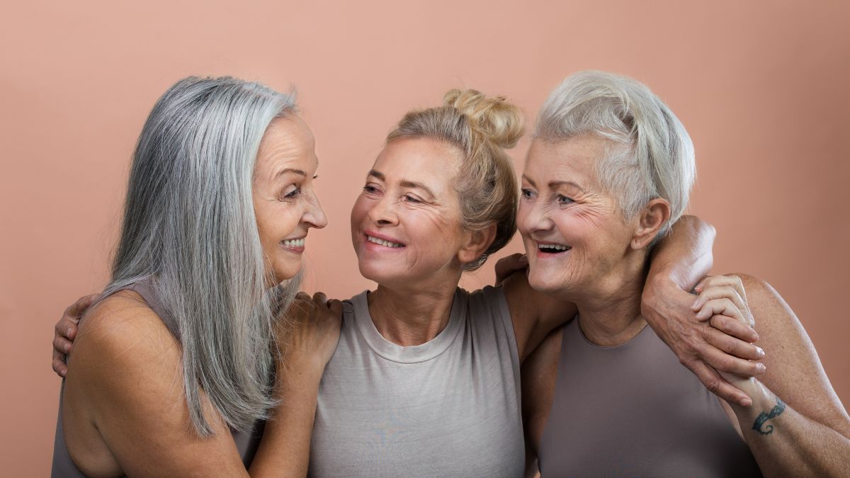 Three older white women smiling with their arms around one another