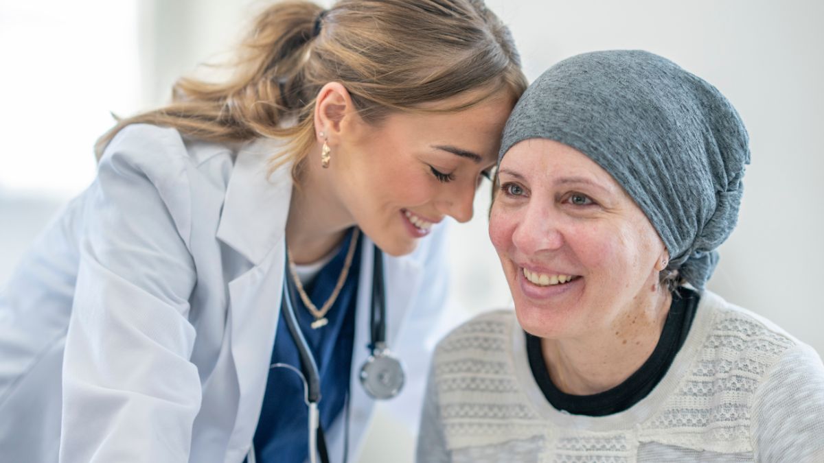 A white female doctor placing her head on a smiling breast cancer patient