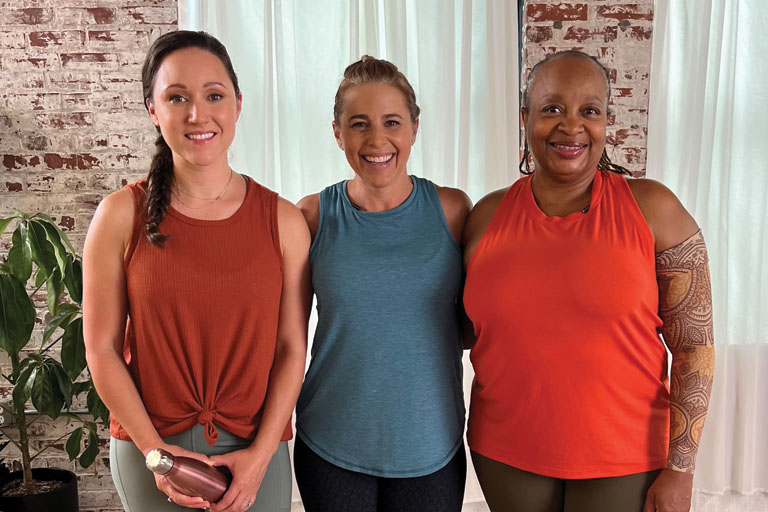 Two white women and a Black woman smiling in the studio after a workout