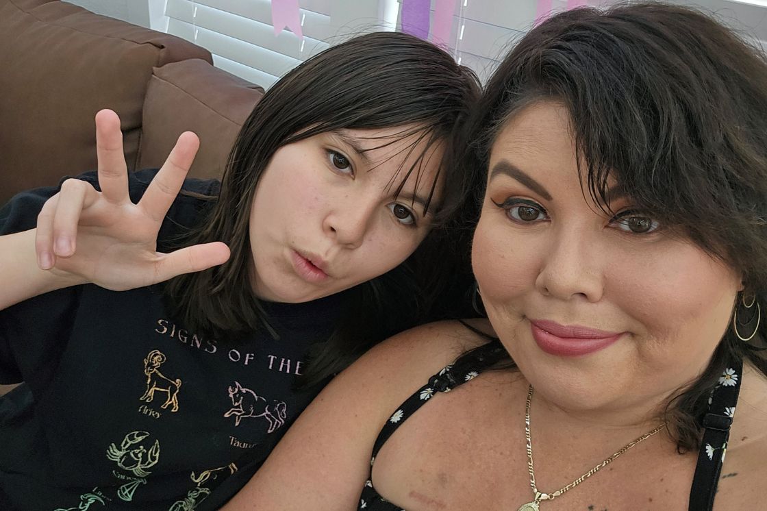 Deb Ontiveros sits on her couch with her daughter signing peace right next to her.