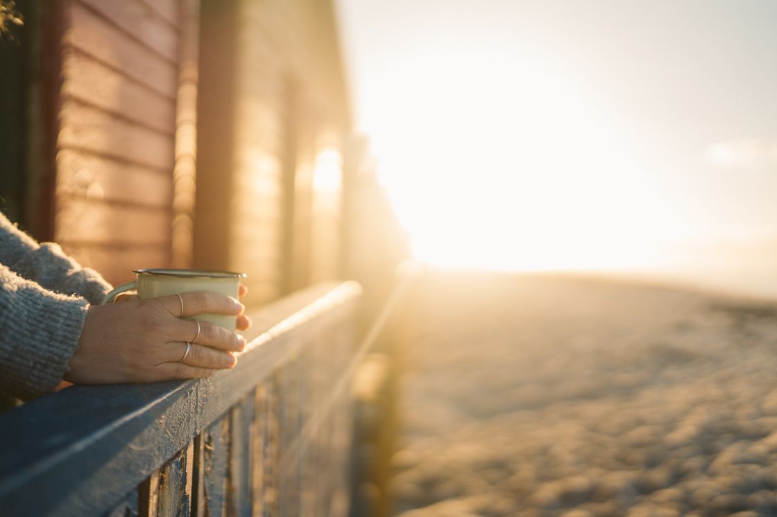 Hands rest against a deck fence, holding a cup of coffee in the morning light.
