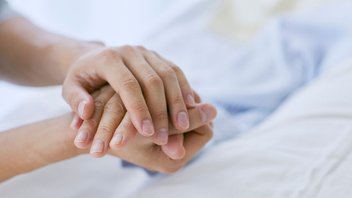 A pair of hands comforts a person confined to bed.