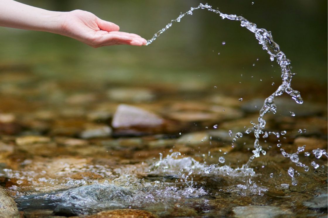 A hand tosses water in a beautiful, translucent stream where many pebbles line the bottom.