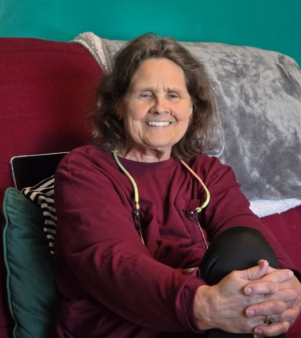Her hands clasped around her knee, Sherry Lawson wears a big smile as she sits on her sofa.