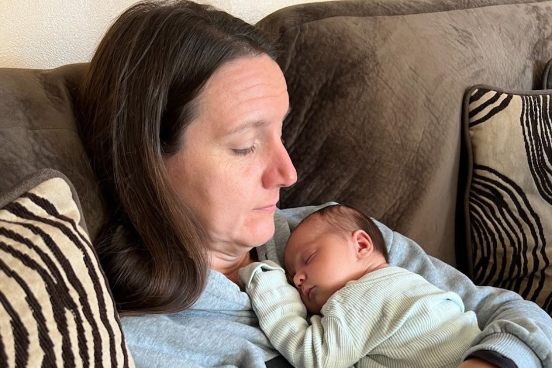 Ericka Toth holds her tiny baby granddaughter close to her chest as she reclines on her sofa.