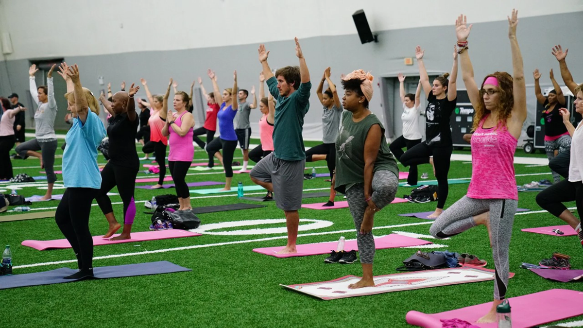 A diverse group of adults doing yoga on an indoor turf field