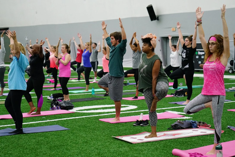 A diverse group of adults doing yoga on an indoor turf field