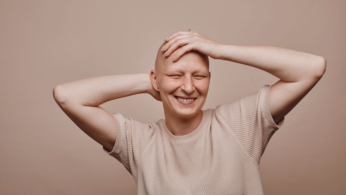 A bald woman smiles as she rubs her hands on her head